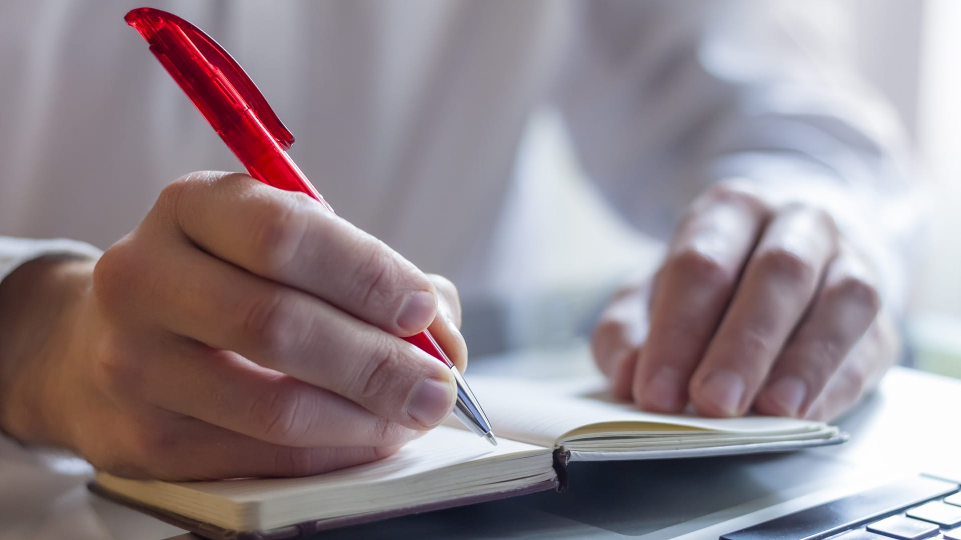 Man writing in a small book using a red pen